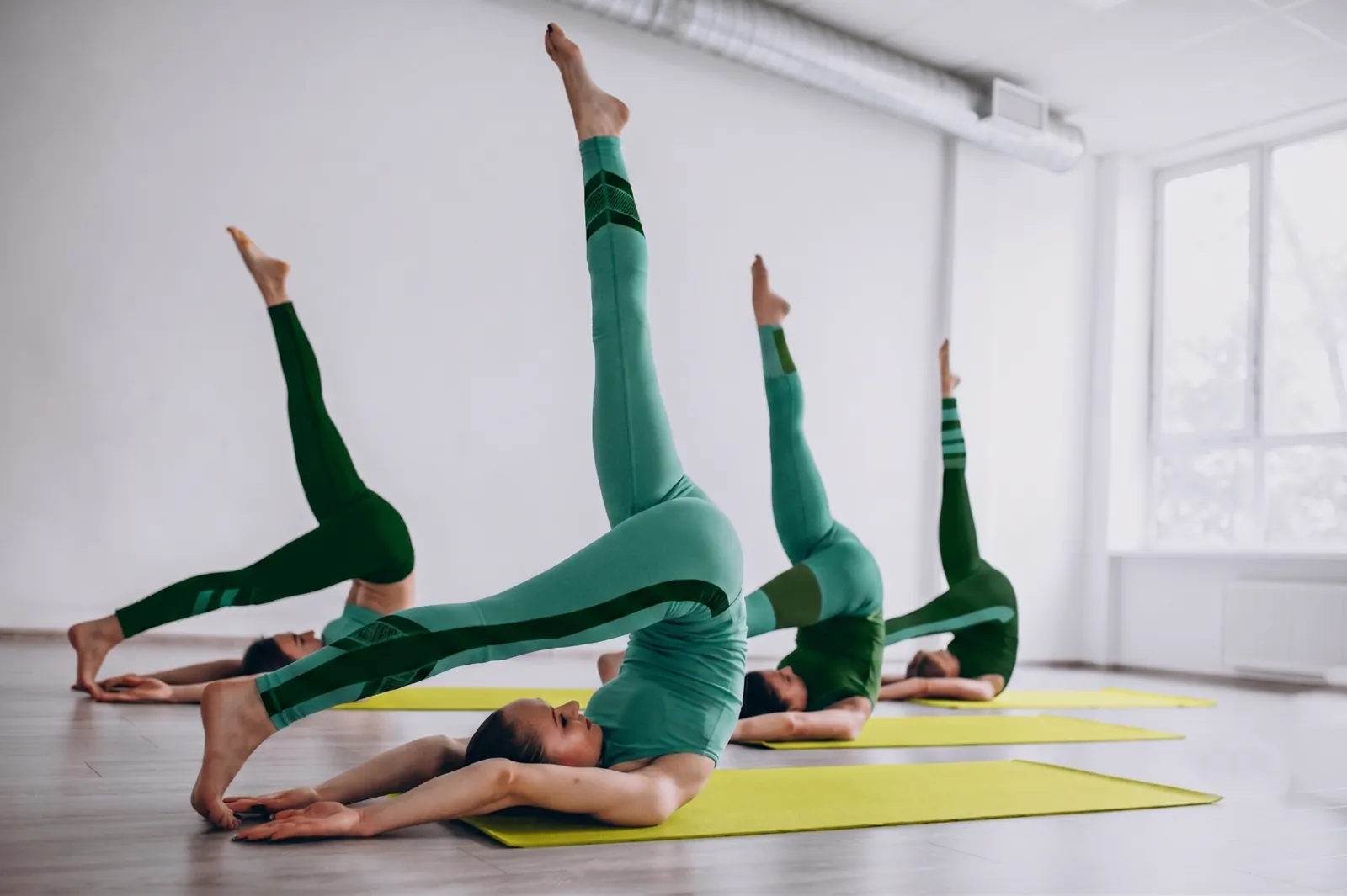 Gruppo di persone in abbigliamento verde esegue esercizi di Pilates su tappetini gialli in uno studio luminoso