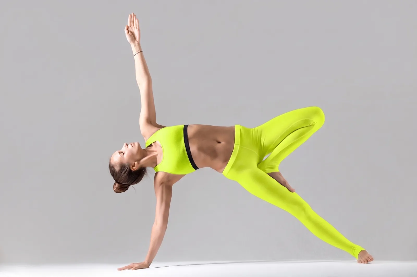 Donna in abbigliamento sportivo giallo neon esegue una variante della posizione della plancia laterale